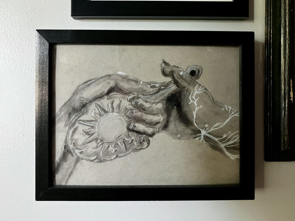 A framed charcoal drawing of two hands, one handing an ornate mirror to the other. The one taking the mirror at lichtenberg figure scars going up the arm.