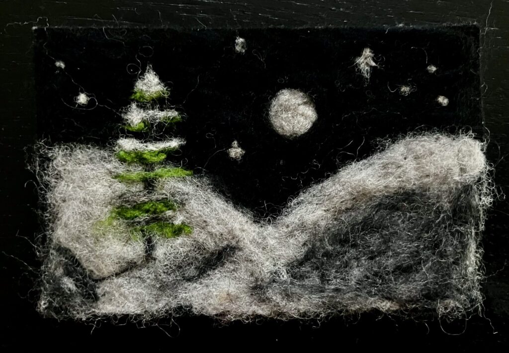 A needlefelted scene of a single pine tree in a snowy landscape at night.