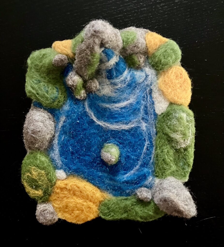 A needlefelted scene of a pond and waterfall surrounded by rocks and greenery.