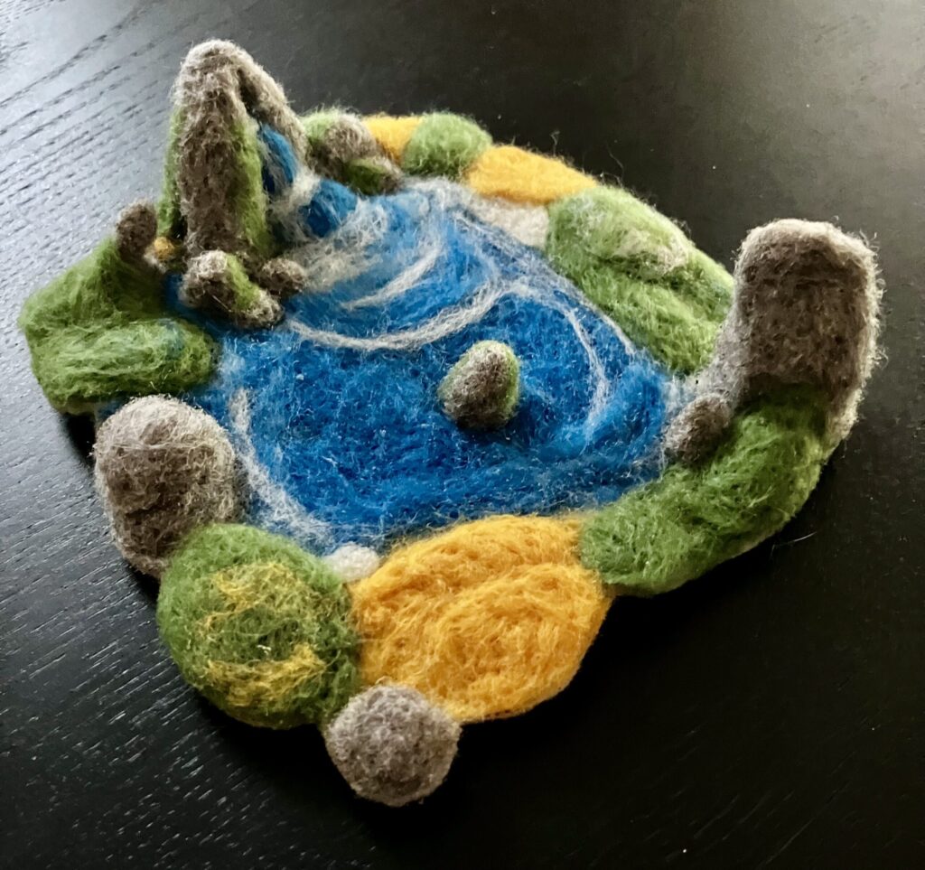 A needlefelted scene of a pond and waterfall surrounded by rocks and greenery.