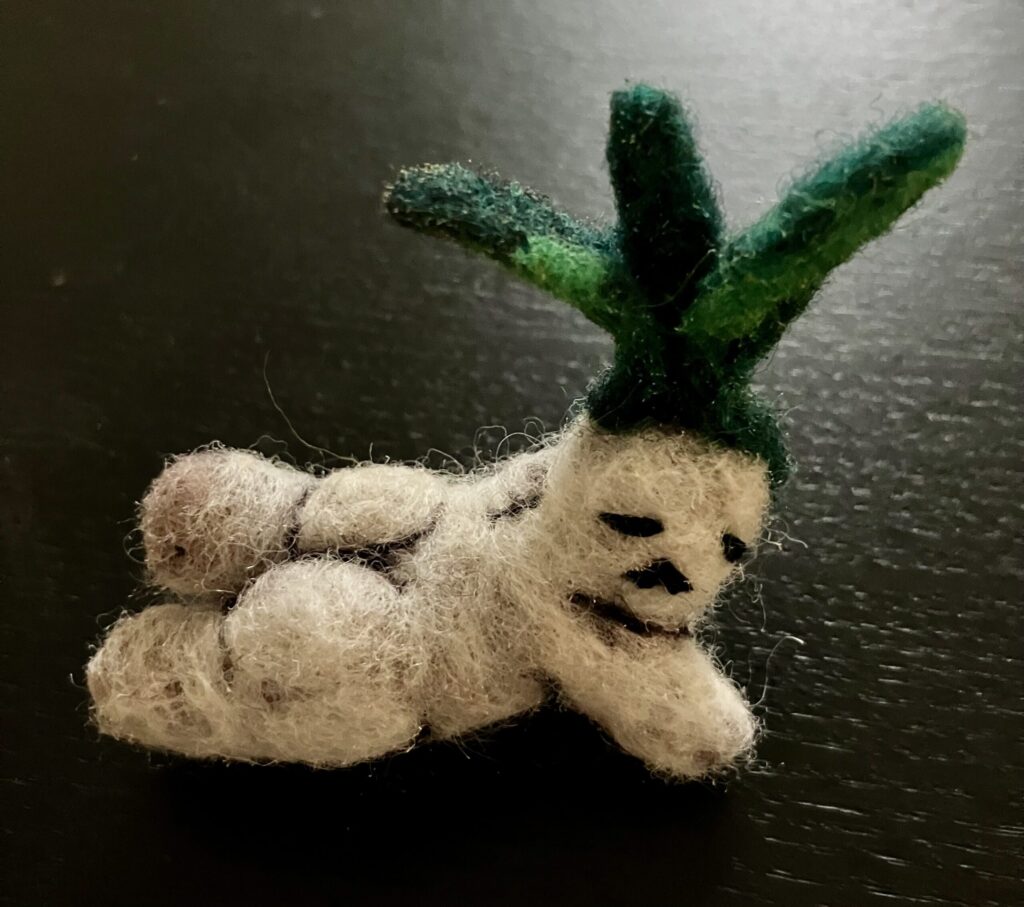 A needlefelted mandrake laying on its stomach.