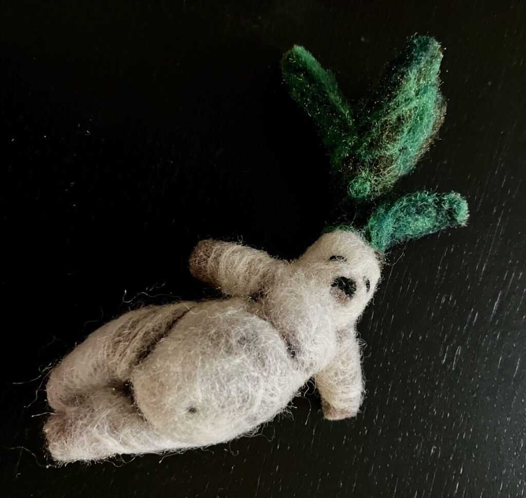 A needlefelted mandrake laying on its side.