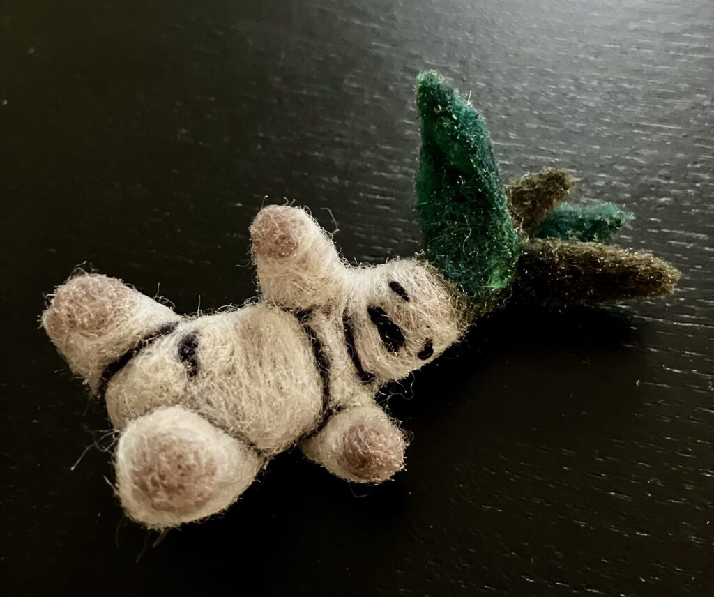 A needlefelted mandrake on its back, struggling to get up.