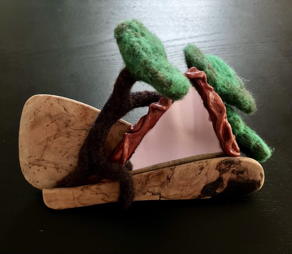 An assemblage of a broken wooden spatula, a piece of mirror, and a needlefelted tree.