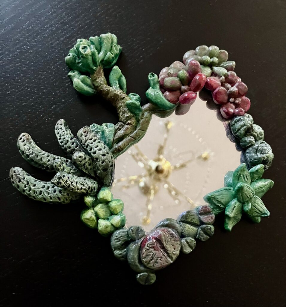 A mirror with sculpted and painted succulents bordering it.