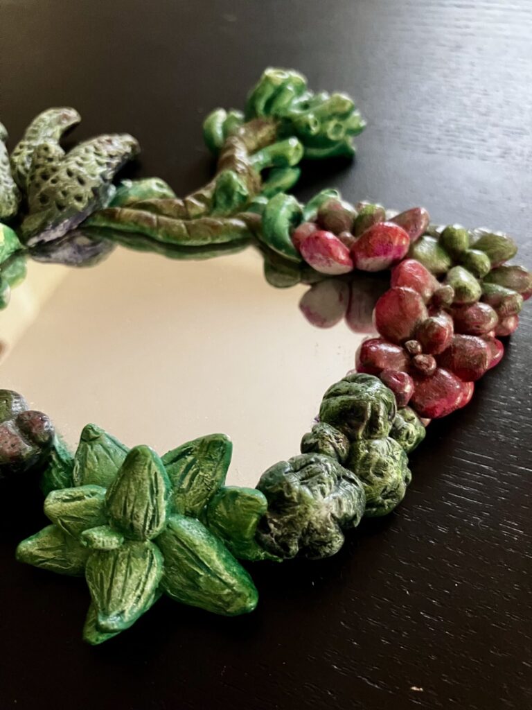A mirror with sculpted and painted succulents bordering it.