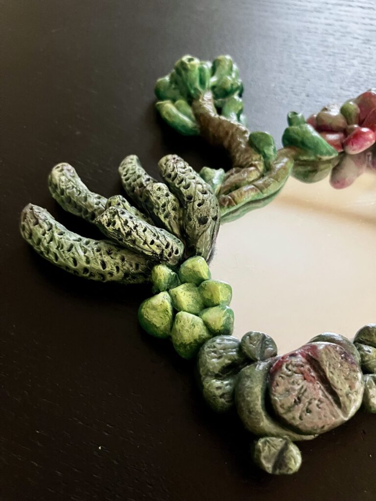 A mirror with sculpted and painted succulents bordering it.
