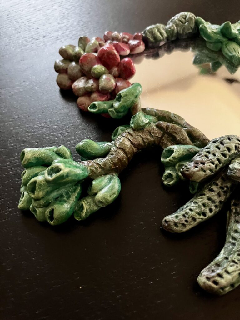 A mirror with sculpted and painted succulents bordering it.
