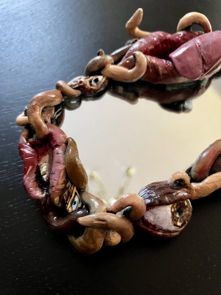 A mirror with a border of sculpted mouths, eyes, and fleshy tendrils.