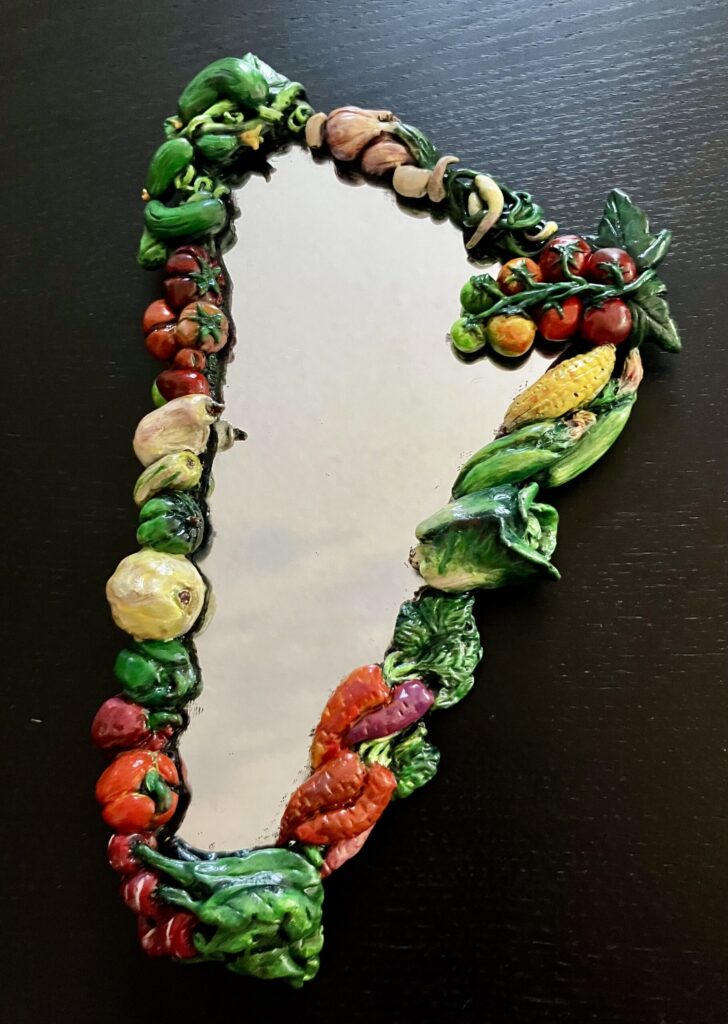 A photo of a mirror bordered by painted, sculpted vegetables.