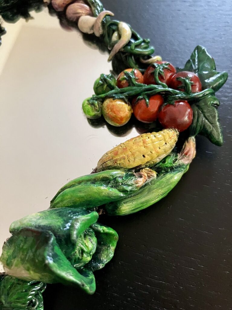 A close up of a mirror bordered by painted, sculpted vegetables.