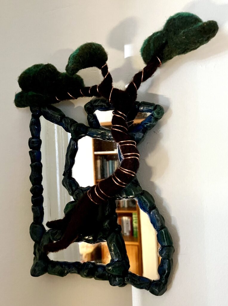 A photo of an assemblage of mirrors with sculpted faux stone borders and a needlefelted bonsai tree wired to them.
