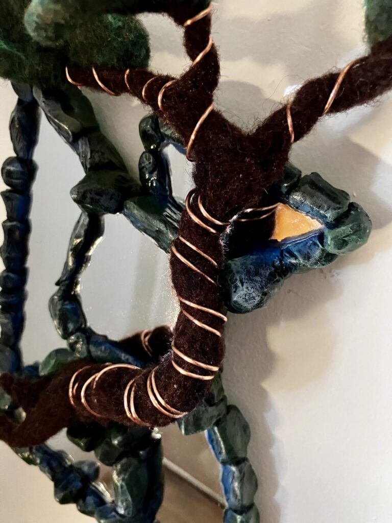 A photo of an assemblage of mirrors with sculpted faux stone borders and a needlefelted bonsai tree wired to them.