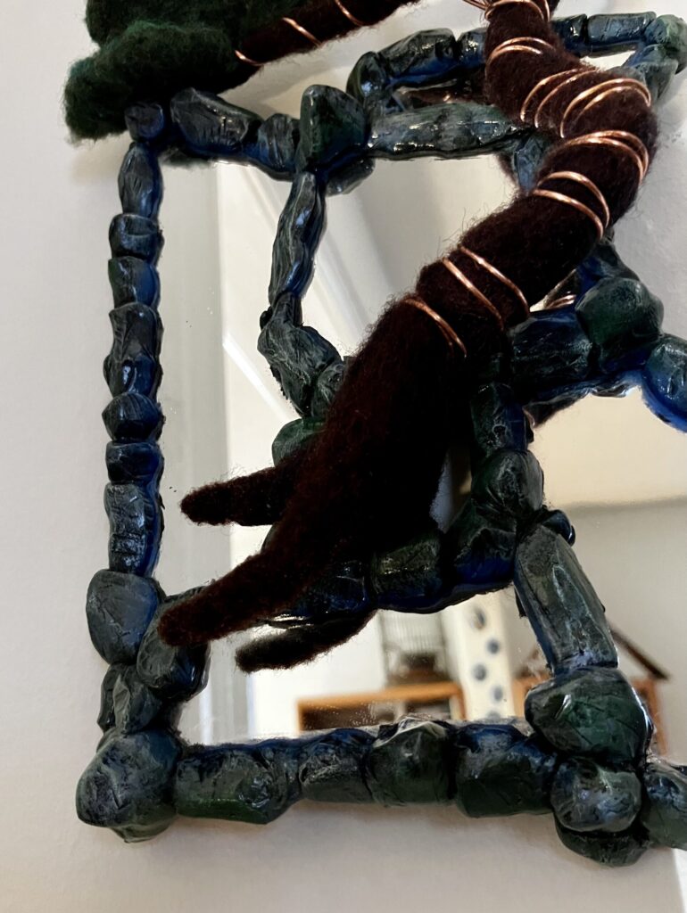 A photo of an assemblage of mirrors with sculpted faux stone borders and a needlefelted bonsai tree wired to them.