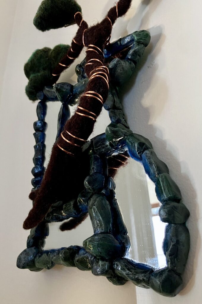 A photo of an assemblage of mirrors with sculpted faux stone borders and a needlefelted bonsai tree wired to them.