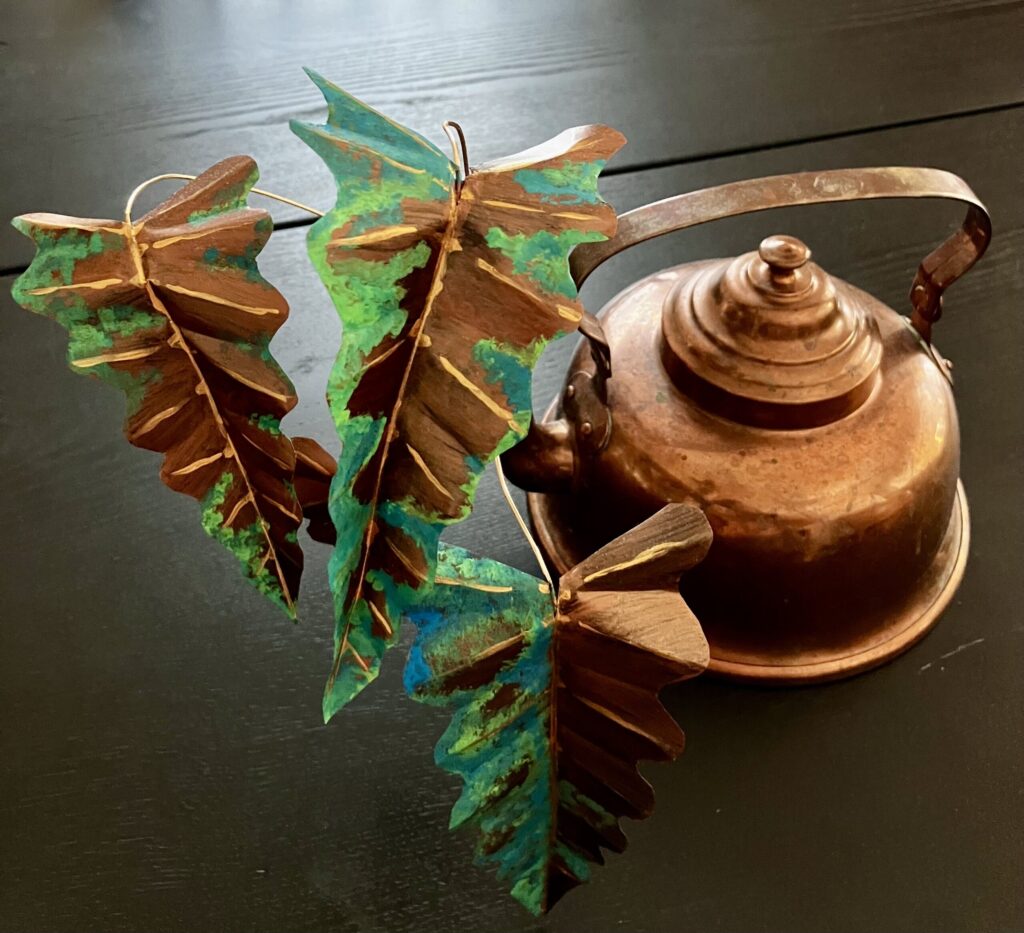 A photo of a sculpted copper colored alocasia growing out of a copper kettle.