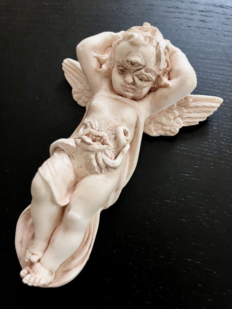 A cherub statue that has been given a mouth growing on its stomach and a third eye.