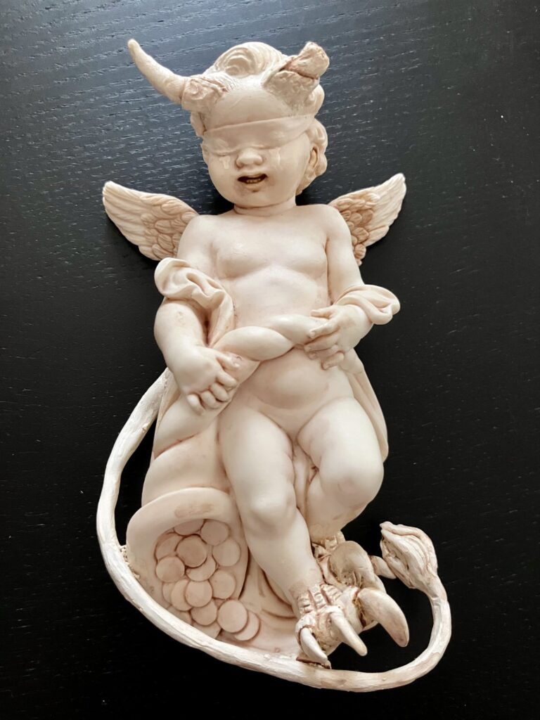 A cherub statue that has been given devil horns and tail.
