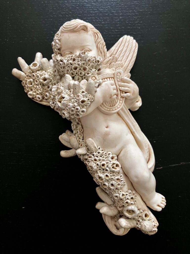 A statue of a cherub with barnacles growing over its surface.