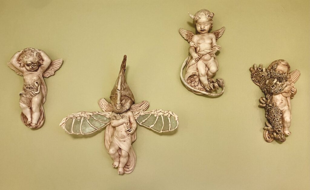 A photo of four cherub statues with have been modified. One is covered in barnacles, one has a beetle head and wings, one has horns and a devil tail, and one has grown a mouth and tendrils on its stomach and a third eye.