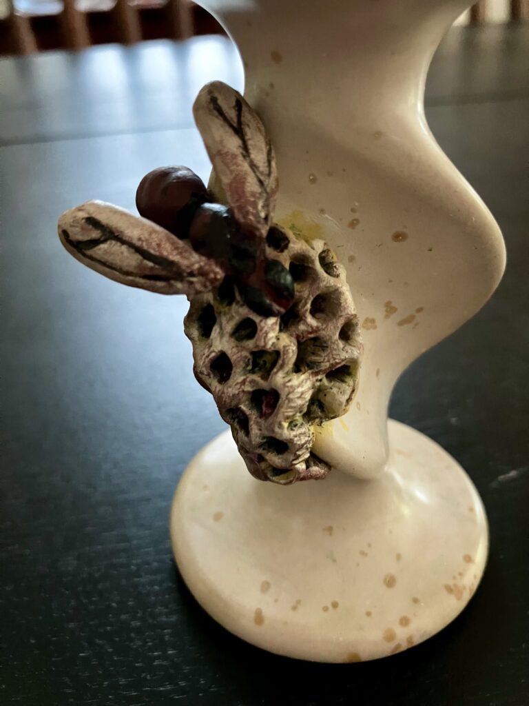 A candlestick with a sculpted wasp and nest on it.