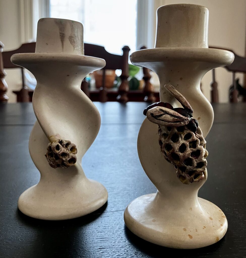 A pair of candlesticks, one with a sculpted wasp nest, and one with a sculpted wasp and nest on them.