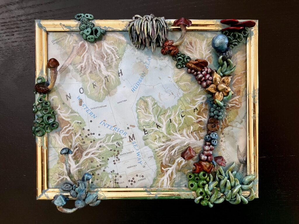 A photo of a framed map of prehistoric North America with sculpted mushrooms growing on the outside of the glass.